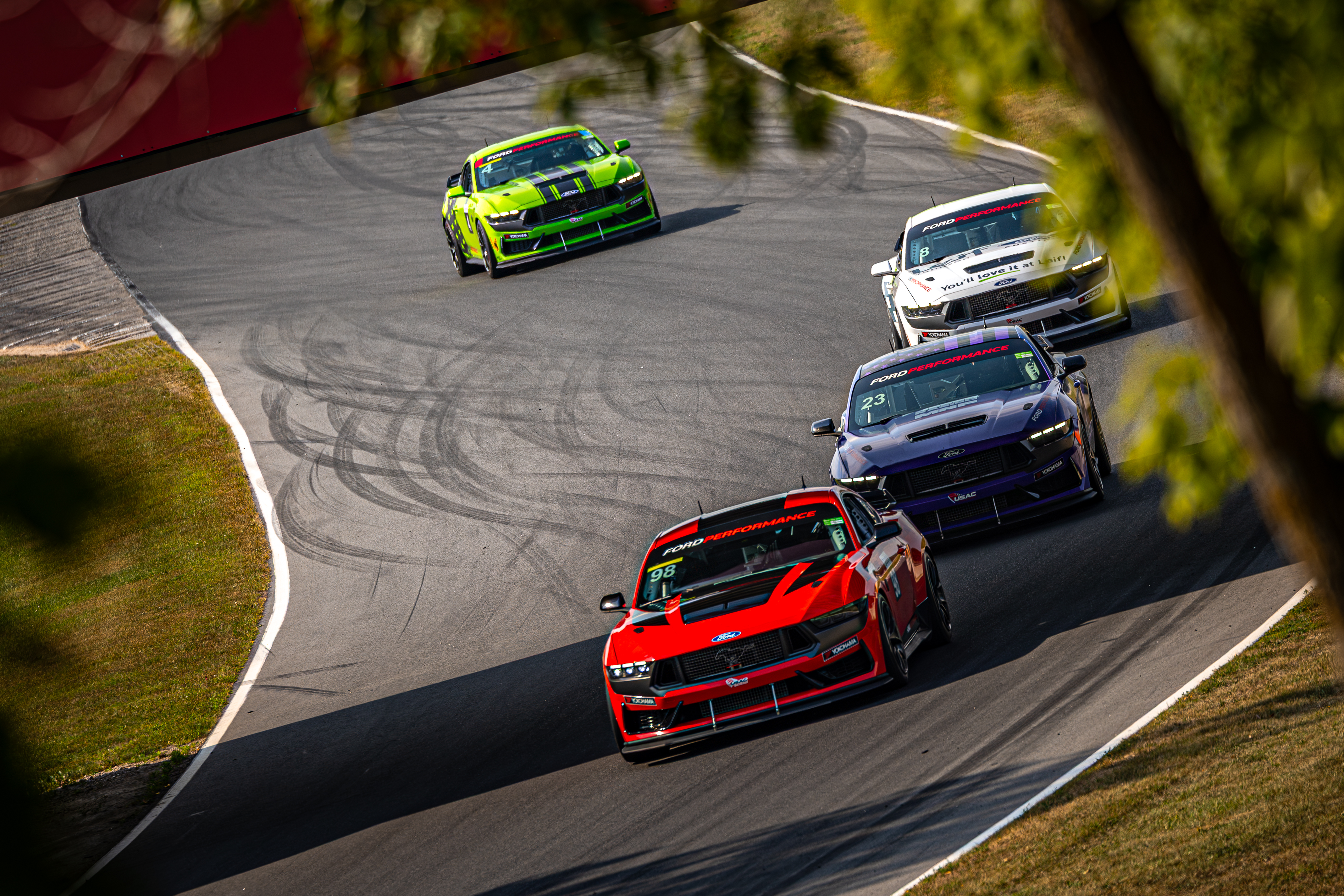 Red, navy, white, and lime green Mustangs race around a track.